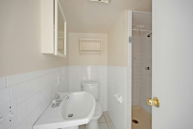 bathroom featuring sink, tile patterned flooring, toilet, tiled shower, and tile walls