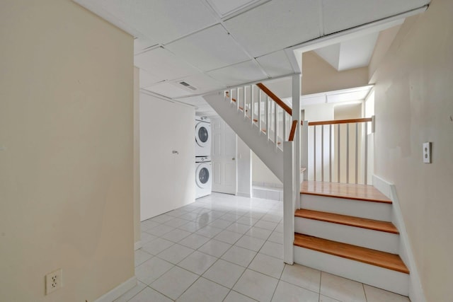 staircase featuring a paneled ceiling, tile patterned floors, and stacked washer and clothes dryer