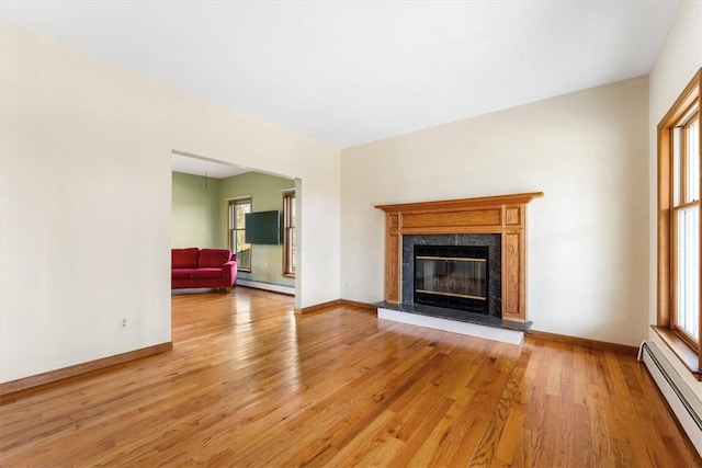 unfurnished living room with light wood-type flooring, baseboard heating, and a premium fireplace