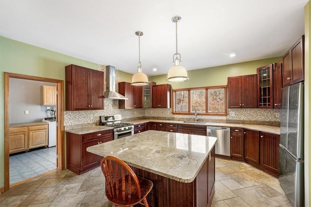 kitchen featuring wall chimney exhaust hood, stainless steel appliances, sink, a kitchen island, and hanging light fixtures