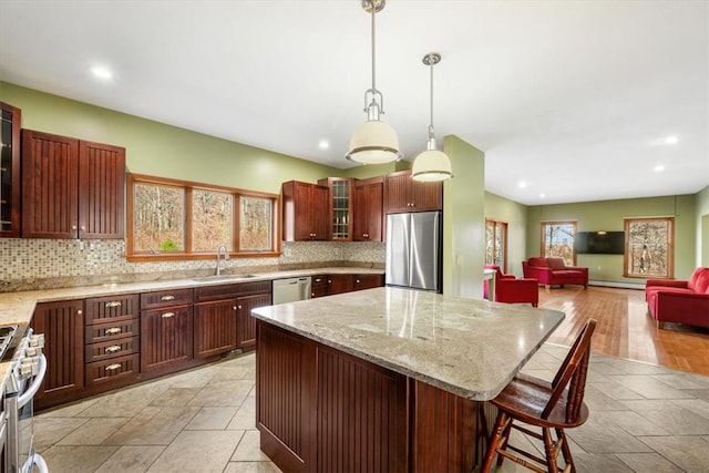 kitchen with backsplash, appliances with stainless steel finishes, decorative light fixtures, a kitchen island, and a kitchen bar