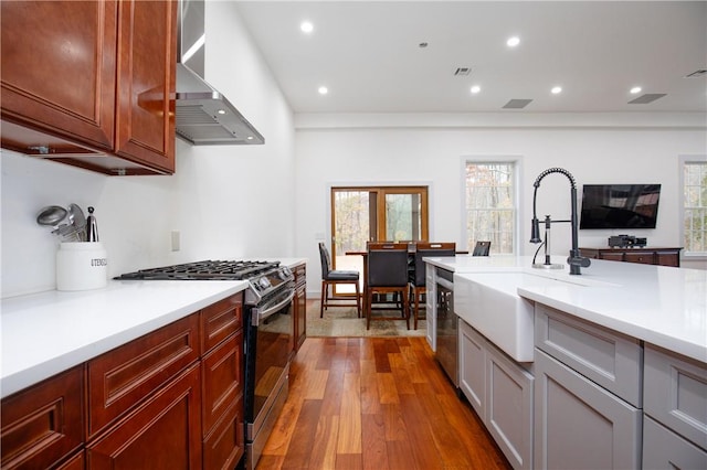 kitchen featuring stainless steel range with gas cooktop, dark hardwood / wood-style flooring, wall chimney exhaust hood, and sink