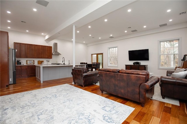 living room featuring beamed ceiling, light hardwood / wood-style floors, and sink