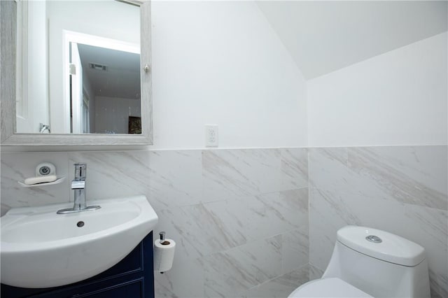 bathroom with vanity, toilet, lofted ceiling, and tile walls