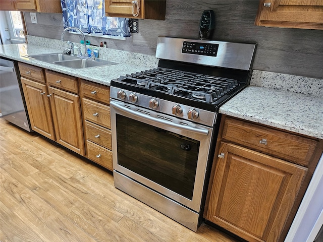 kitchen with light stone countertops, appliances with stainless steel finishes, light hardwood / wood-style flooring, and sink