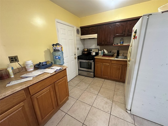 kitchen with white fridge, light tile patterned floors, gas stove, tasteful backsplash, and sink