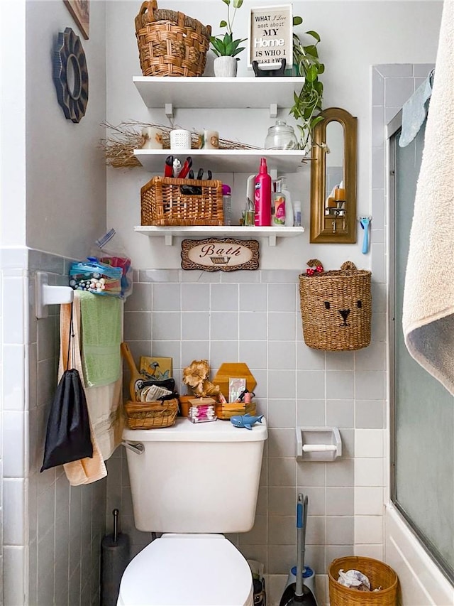 bathroom featuring toilet, tile walls, and bath / shower combo with glass door