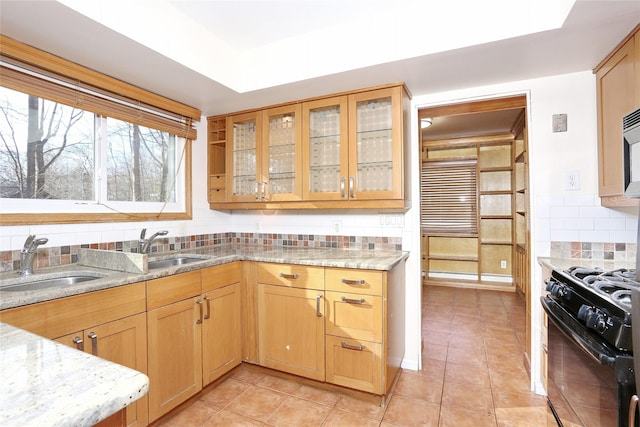 kitchen with light stone countertops, tasteful backsplash, black range oven, sink, and light tile patterned flooring