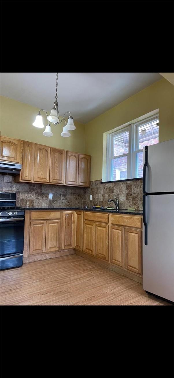 kitchen featuring decorative backsplash, stainless steel fridge, exhaust hood, electric range, and a chandelier