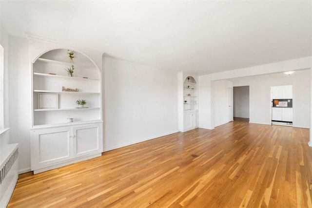 unfurnished living room featuring radiator heating unit, light hardwood / wood-style floors, and built in features