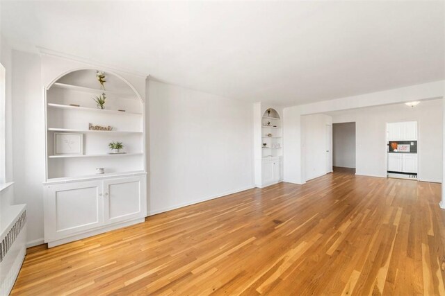 19 Old Mamaroneck Rd Unit 6D, White Plains, NY 10605 - unfurnished living room featuring radiator, light wood finished floors, and built in shelves
