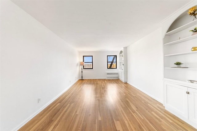 unfurnished room with radiator heating unit, light wood-type flooring, and built in shelves