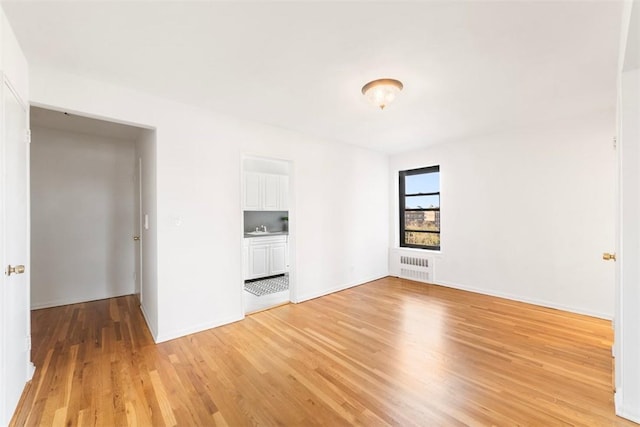 unfurnished room with radiator heating unit, light wood-type flooring, and sink