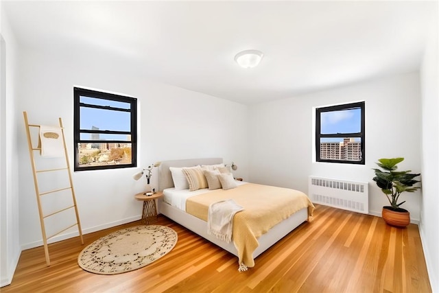 bedroom with hardwood / wood-style floors, radiator, and multiple windows