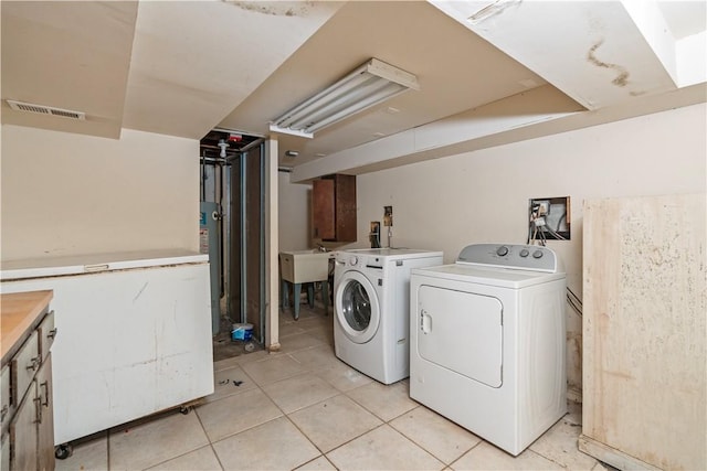 clothes washing area featuring washing machine and dryer, sink, light tile patterned flooring, and gas water heater