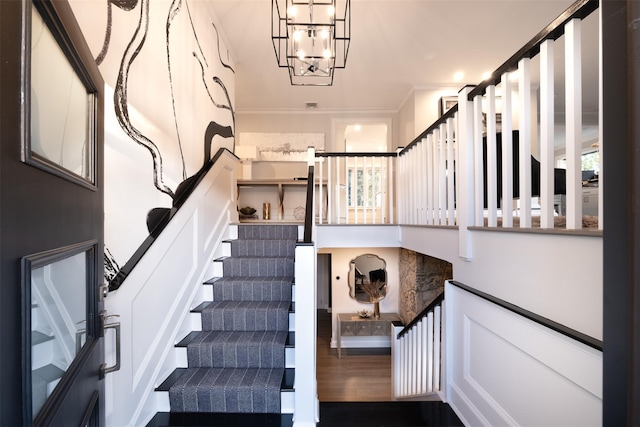 staircase featuring a notable chandelier, ornamental molding, and wood finished floors