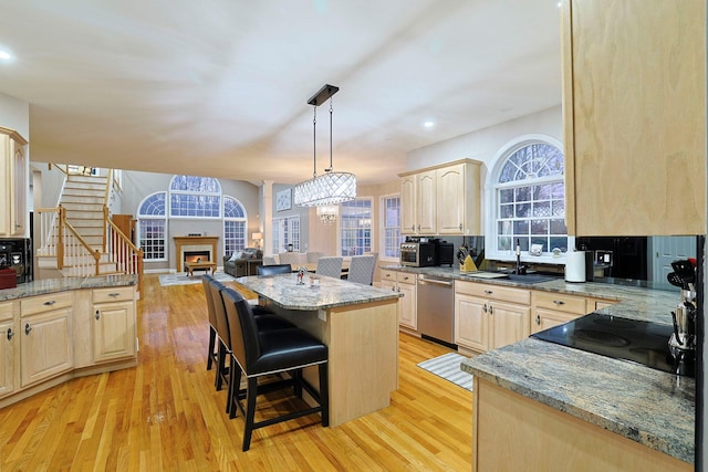 kitchen with stainless steel dishwasher, a center island, light brown cabinetry, and light hardwood / wood-style flooring