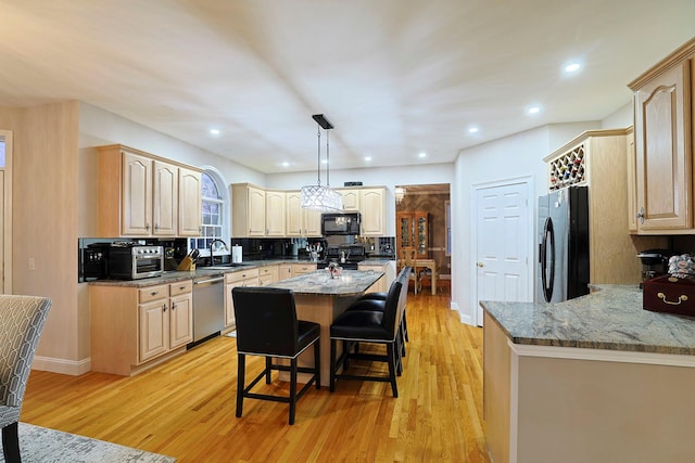 kitchen featuring a kitchen bar, black appliances, light hardwood / wood-style flooring, a center island, and hanging light fixtures