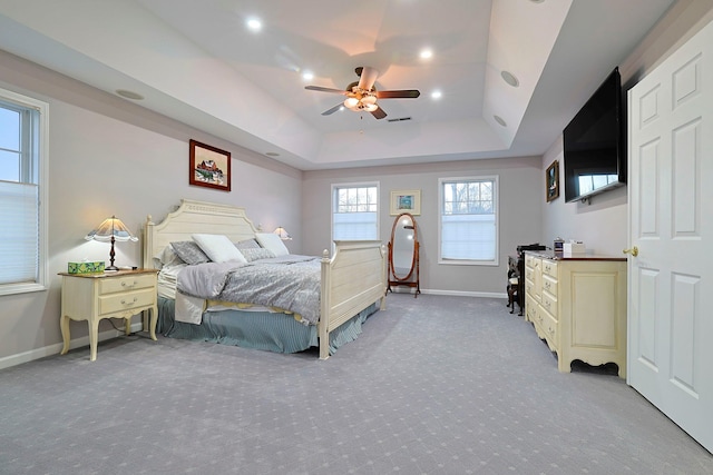 bedroom featuring a raised ceiling, light carpet, and ceiling fan