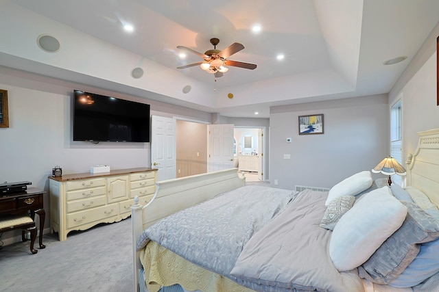 bedroom featuring ceiling fan, light colored carpet, connected bathroom, and a tray ceiling