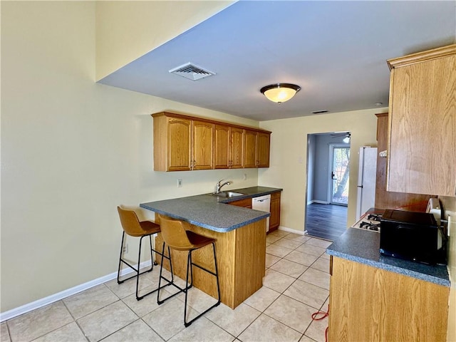 kitchen featuring sink, kitchen peninsula, white appliances, a breakfast bar area, and light tile patterned floors