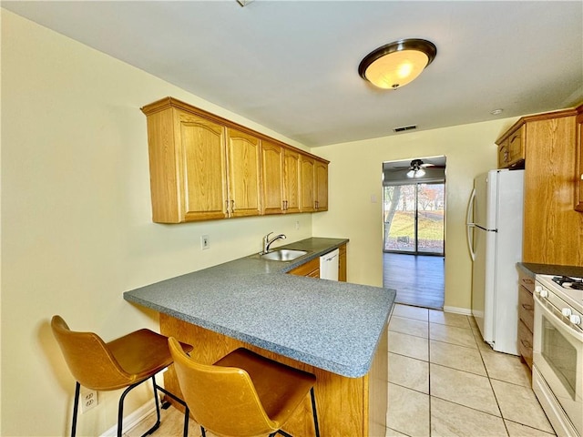 kitchen with a kitchen bar, kitchen peninsula, white appliances, sink, and light tile patterned floors