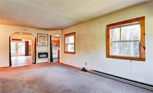 unfurnished living room featuring heating unit, a wealth of natural light, carpet, and a baseboard heating unit