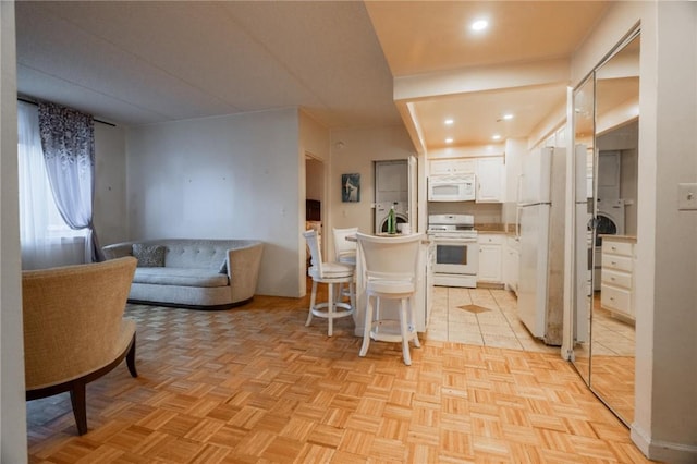 kitchen featuring a kitchen bar, light parquet floors, white cabinets, and white appliances