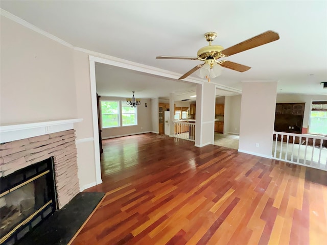 unfurnished living room featuring ceiling fan with notable chandelier, a stone fireplace, wood-type flooring, and ornamental molding