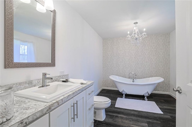 bathroom with a bathtub, vanity, an inviting chandelier, hardwood / wood-style floors, and toilet