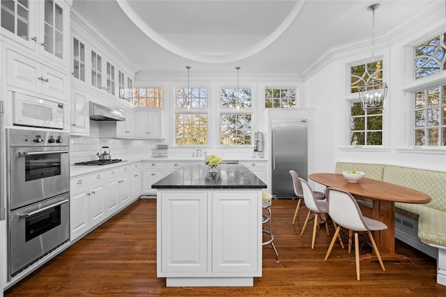 kitchen with a tray ceiling, breakfast area, appliances with stainless steel finishes, white cabinets, and wall chimney exhaust hood