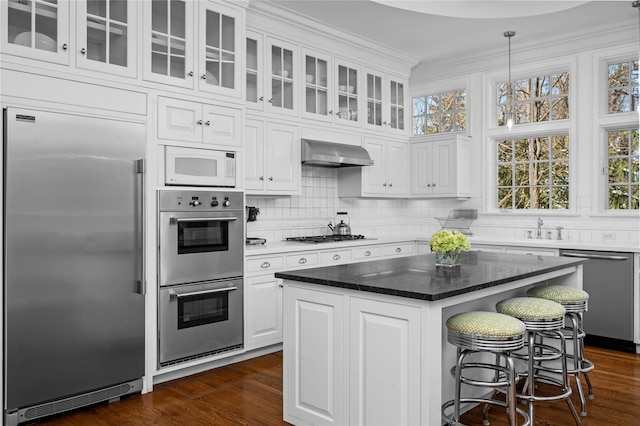 kitchen featuring stainless steel appliances, white cabinetry, wall chimney range hood, backsplash, and dark wood-style floors