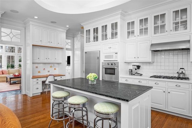 kitchen featuring wall chimney range hood, appliances with stainless steel finishes, white cabinets, and dark wood-type flooring