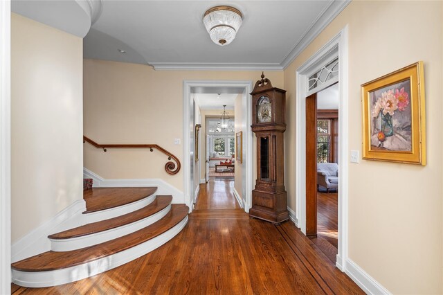 hallway with dark wood-type flooring, stairway, baseboards, and an inviting chandelier