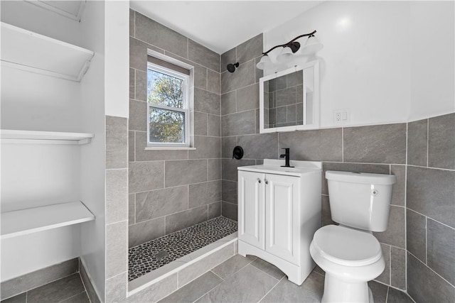 bathroom with a tile shower, vanity, toilet, and tile walls