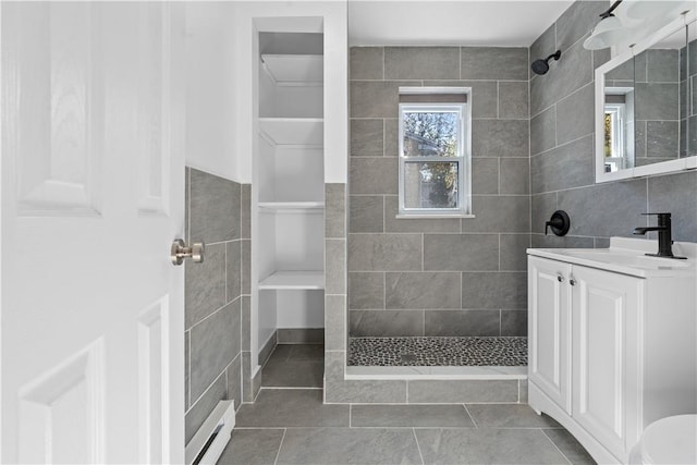 bathroom with a tile shower, tile patterned flooring, a baseboard heating unit, vanity, and tile walls