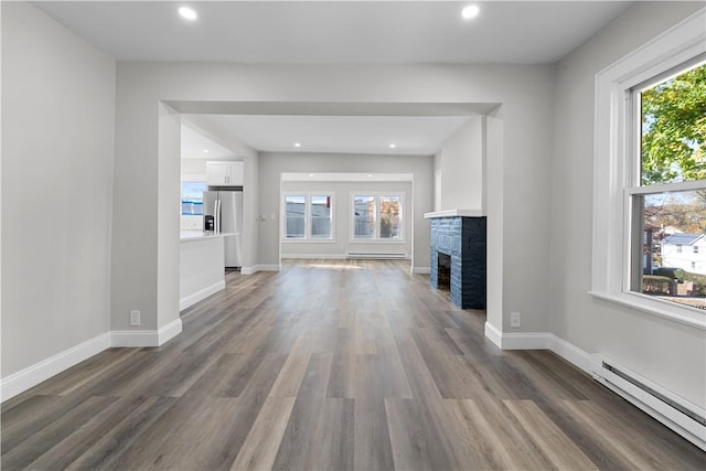 unfurnished living room featuring a fireplace, baseboard heating, a wealth of natural light, and dark wood-type flooring