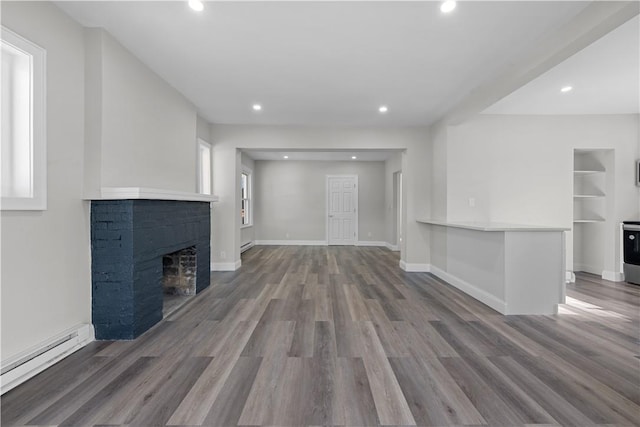 unfurnished living room with hardwood / wood-style flooring, a brick fireplace, and a baseboard heating unit