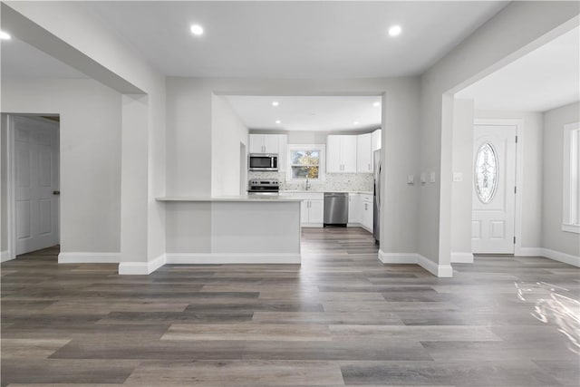 interior space featuring kitchen peninsula, backsplash, stainless steel appliances, wood-type flooring, and white cabinetry