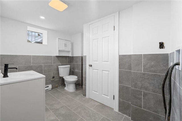 bathroom with a baseboard heating unit, tile patterned floors, toilet, vanity, and tile walls