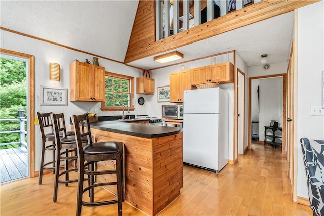 kitchen with light wood-type flooring, a textured ceiling, vaulted ceiling, white refrigerator, and a breakfast bar area