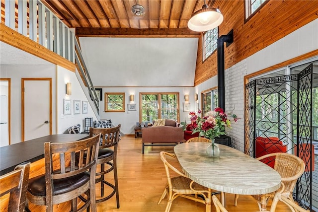 dining space featuring a wood stove, high vaulted ceiling, light hardwood / wood-style flooring, beam ceiling, and wood ceiling