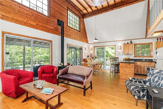 living room featuring beamed ceiling, plenty of natural light, a wood stove, and high vaulted ceiling