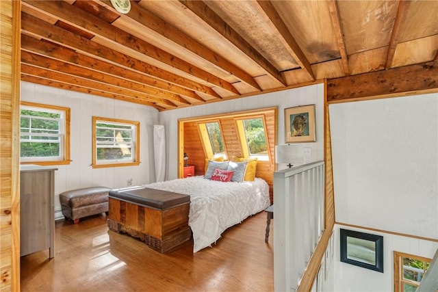 bedroom featuring wood walls, beam ceiling, light hardwood / wood-style flooring, and multiple windows