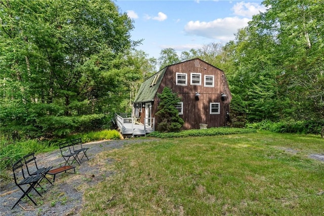 exterior space featuring a front yard, a wooden deck, and a gambrel roof