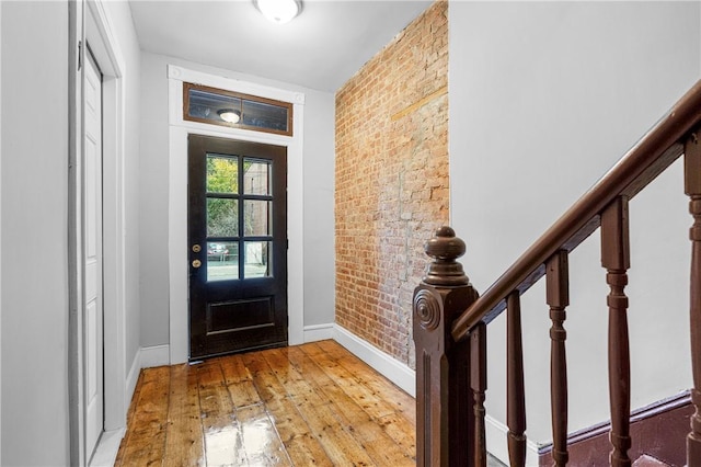 foyer with wood-type flooring and brick wall