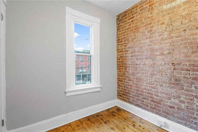 spare room featuring hardwood / wood-style floors and brick wall