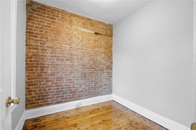 empty room with hardwood / wood-style floors and brick wall