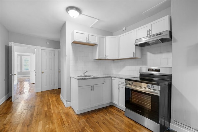 kitchen featuring decorative backsplash, white cabinetry, stainless steel range, and light hardwood / wood-style flooring