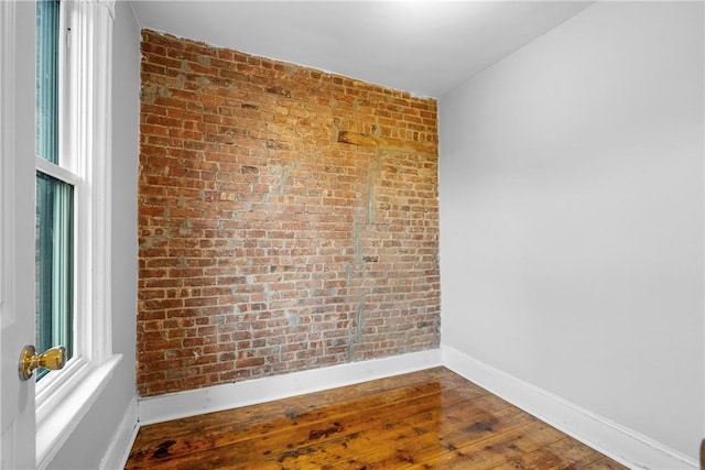 empty room featuring wood-type flooring and brick wall